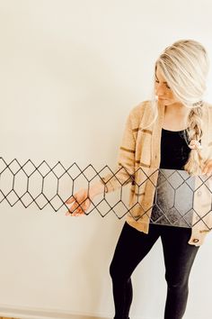 a woman standing in front of a wall holding onto a piece of wire that is connected to the wall