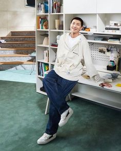 a young man sitting on top of a desk next to a book shelf