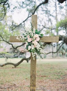 a cross decorated with flowers and greenery in front of an oak tree at a wedding