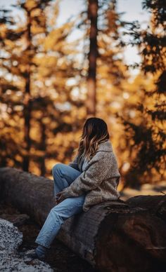 a woman sitting on top of a log in the woods