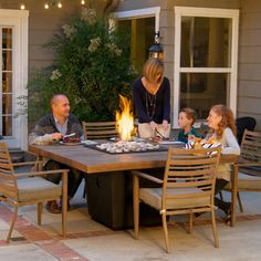 a family sitting around a fire pit with food on the table in front of them