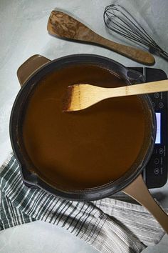 a wooden spoon in a pot filled with liquid next to a whisk and spatula