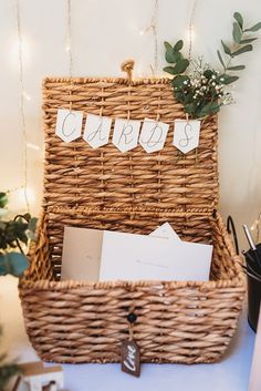 a wicker basket filled with cards and envelopes next to a christmas tree on a table