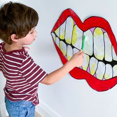 a young boy holding a toothbrush in front of a wall with a mouth painted on it