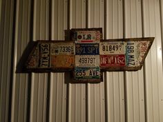 an old license plate cross hanging on a metal wall in front of a corrugated building