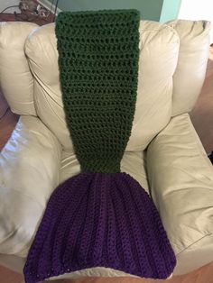 a purple and green knitted mermaid tail sitting on a white couch next to a pillow