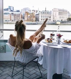 a woman sitting at a table in front of a window with food and drinks on it