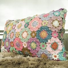 a multicolored crocheted pillow sitting on top of a fur covered bench