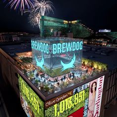 fireworks light up the night sky above a building with an advertisement on it's roof