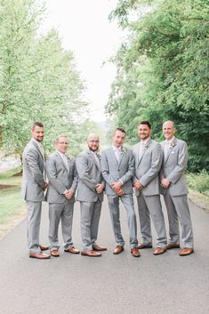 a group of men in grey suits standing next to each other on a road surrounded by trees