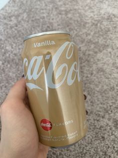 a person holding up a can of coca - cola on the floor in front of carpet