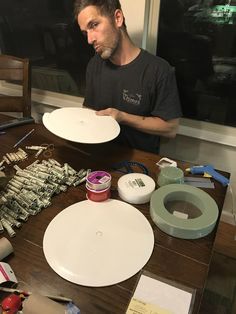 a man is working on some art work with paper plates and paintbrushes in front of him