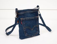 This stylish crossbody bag is handmade from upcycled blue jeans, making it both eco-friendly and unique. The interior is lined with cotton fabric, secured with a magnetic snap closure. It features two handy pockets--one on the exterior and one on the interior (both repurposed jean pockets) to keep your essentials organized. BAG DIMENSIONS: Approximate Size: 8.5"H (21.5 cm) x 7"W (17.75 cm) x 1.5"D (3.75 cm) Shoulder Strap Drop: Adjustable from 15" to 26" (38 cm to 66 cm) FEATURES: Exterior: Recy Jean Pockets, Denim Projects, Gray Interior, Phone Bag, Shoulder Purse, Levis Jeans, Cross Body Handbags, Purses And Handbags, Crossbody Bag