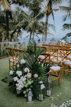 an outdoor ceremony setup with chairs, flowers and greenery on the grass near palm trees