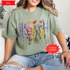 🌺🌷Embrace the enchanting beauty of nature with our Pressed Wildflower Vintage Cottagecore T-shirt. This charming piece features a delightful vintage floral design that captures the essence of wild meadows and secret gardens. Perfect for the free-spirited soul, this t-shirt effortlessly blends boho chic with fairycore whimsy. Available in a range of soft, dreamy hues including white, ivory, peachy, banana, chambray, bay, blossom, and orchid, this versatile top complements any style. The Custom Spring Fairycore Cotton Tops, Fairycore Short Sleeve Tops For Spring, Green Fairycore Tops For Spring, Green Fairycore Summer Top, Green Fairycore Tops For Summer, Green Fairycore Top For Summer, Cottagecore Floral Embroidery T-shirt For Summer, Spring Nature-inspired Short Sleeve T-shirt, Summer Fairycore Crew Neck T-shirt