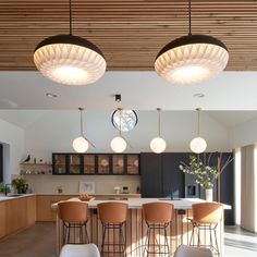 an open kitchen and dining area with bar stools in the foreground, lights hanging from the ceiling