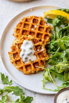 a plate with waffles and greens on it next to a bowl of yogurt