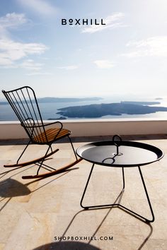 A black metal outdoor rocking chair with bamboo lamellas seat placed on a concrete surface under a clear blue sky