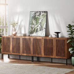 a living room with a large wooden sideboard and potted plants on the floor