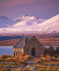 an old church in the middle of nowhere with snow covered mountains behind it and water below