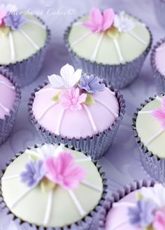 cupcakes decorated with pink and purple flowers on a white tablecloth covered tray