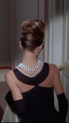 a woman in a black dress with pearls on her neck