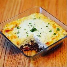 a casserole dish with meat and cheese in it sitting on a wooden table