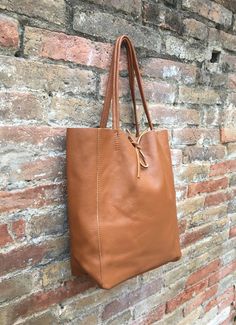 Large tote leather bag in dark CAMEL BROWN. Saddle brown shoulder bag. Tan color natural GENUINE leather. Large enough for books or a laptop, tablet, cosmetics bag etc. Leather shopper. The inside of the bag is not lined (although properly finished!) . We added a small leather pouch on the inner part of the bag (4th pic) The bag can be closed by 2 leather straps attached to each side. Excellent quality soft but strong genuine leather. Width upper part: 41cm - 16 inch Height: 38 cm - 15 inch This Daily Use Cognac Shoulder Bag With Textured Leather, Brown Bags With Leather Lining For Everyday Use, Brown Leather Lined Everyday Bag, Brown Leather Lining Bags For Everyday, Everyday Brown Bags With Leather Lining, Rectangular Brown Leather Backpack For Everyday, Brown Leather Lined Satchel For Everyday Use, Casual Brown Satchel With Leather Lining, Everyday Brown Rectangular Leather Backpack