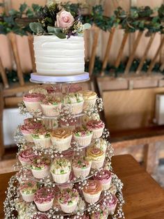 a tiered cake with cupcakes and flowers on top is sitting on a table