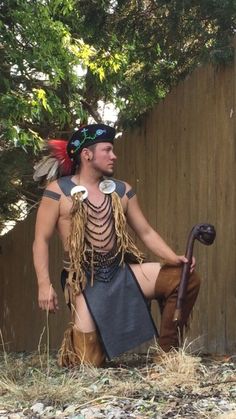 a man dressed in native american garb sitting on the ground next to a fence