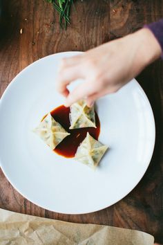 someone is picking up some dumplings on a plate with sauce in the middle and green sprouts next to them