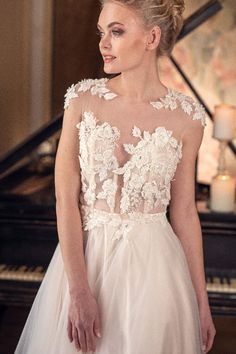 a woman standing in front of a piano wearing a wedding dress with flowers on it