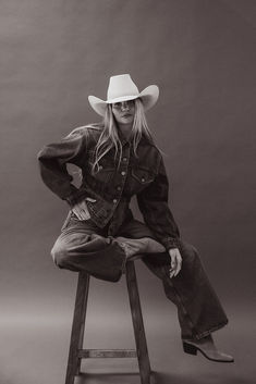 a woman sitting on top of a stool wearing a cowboy hat