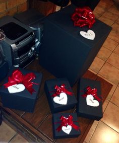 four black boxes with red bows and heart shaped tags on them sitting on a tile floor