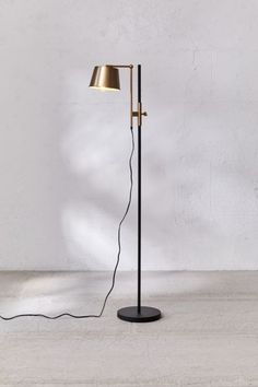 a black floor lamp with a gold shade on the side and a white wall behind it