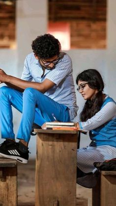 two people sitting on top of wooden blocks with books in front of them and one person writing