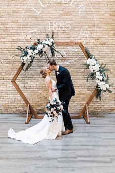 a bride and groom kissing in front of an arch decorated with greenery and flowers