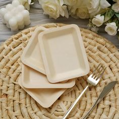 three square plates with forks on a wicker place mat next to white flowers and greenery