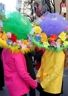 two people walking down the street wearing colorful hats with flowers on it's head