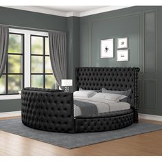 a black bed sitting on top of a hard wood floor next to a large window