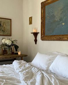 a bed with white sheets and pillows next to a painting on the wall above it