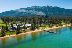 an aerial view of a lake and resort surrounded by pine trees with mountains in the background