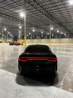 a black sports car is parked in an empty parking garage with yellow poles and lights