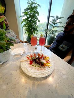 two people sitting at a table with food and drinks in front of them on it