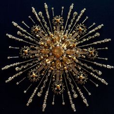 an elaborate brooch with gold and white beads on black background, in the shape of a sunburst