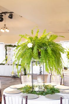 the table is set with white linens, plates and greenery on it for an elegant centerpiece