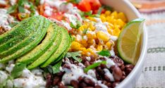 a salad with avocado, black beans, corn, and lime wedges