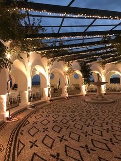 an outdoor dining area at night with lights on the ceiling and tables in the center