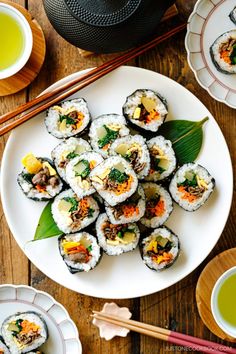 sushi on a plate with chopsticks next to it and two cups of green tea