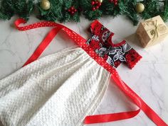 a white dress with red and black bows on it, next to christmas tree decorations